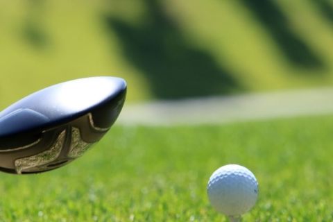 A close up of a golf driver about to this a golf ball off a tee